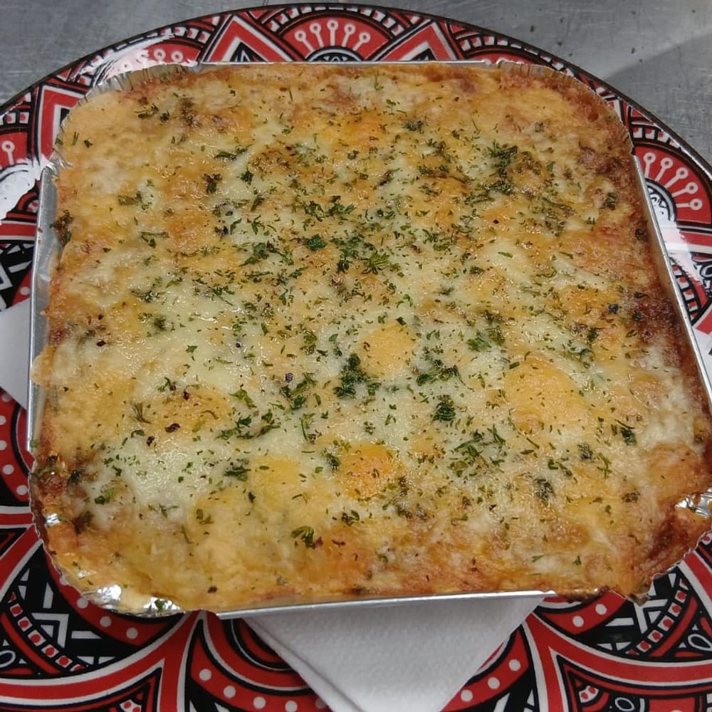 Baked lasagne with a browned, herb-flecked cheese crust, served on a patterned red plate