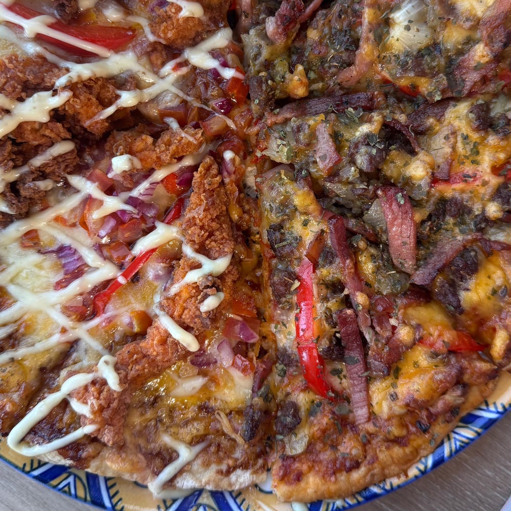 Two half-and-half pizzas: crumbed chicken with mayo drizzle alongside a peppers, bacon and herb topping