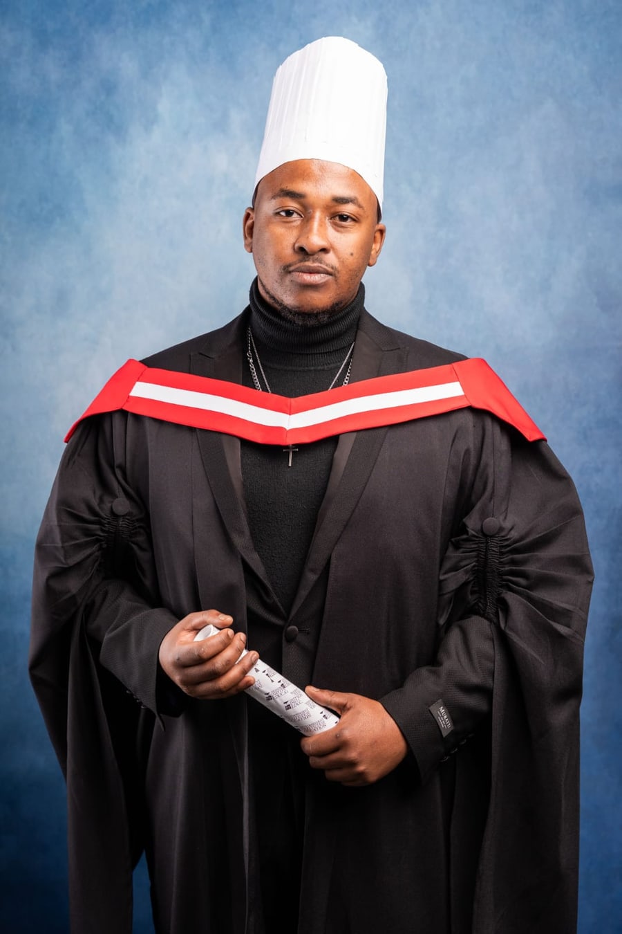 Likolihle Moses in chef's toque and academic gown, holding his Capsicum Culinary Studio certificate