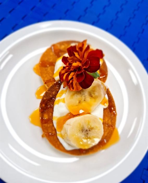 Pancake with cream, sliced banana, caramel and a red edible flower