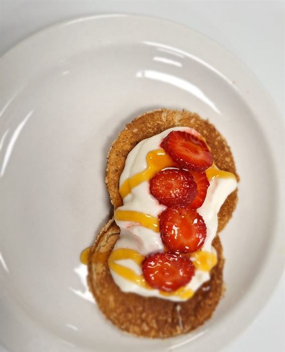 Pancake topped with cream, sliced strawberries and caramel