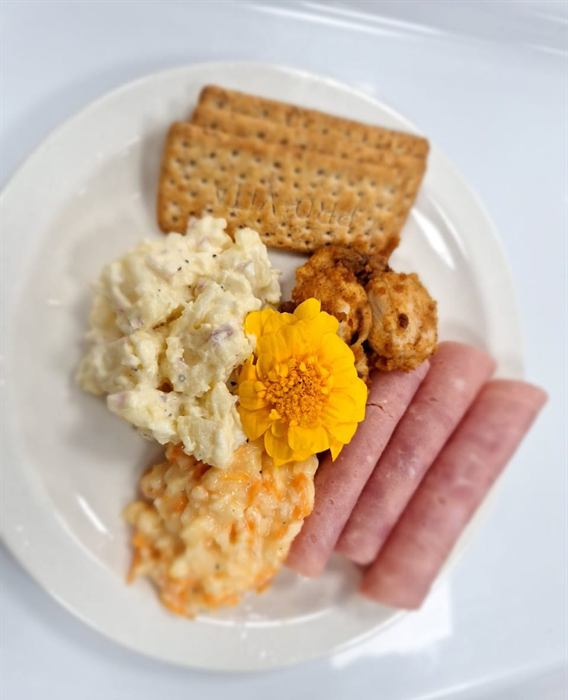Cooked breakfast of egg, rolled ham, hash and crackers with an edible flower