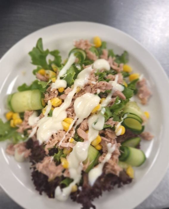 Tuna salad with sweetcorn, cucumber and tomato on dark leaves
