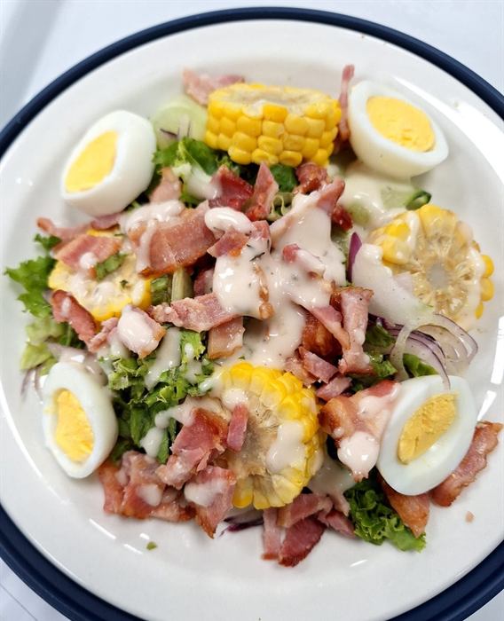 Composed salad with halved boiled eggs, bacon, corn on the cob and dressing