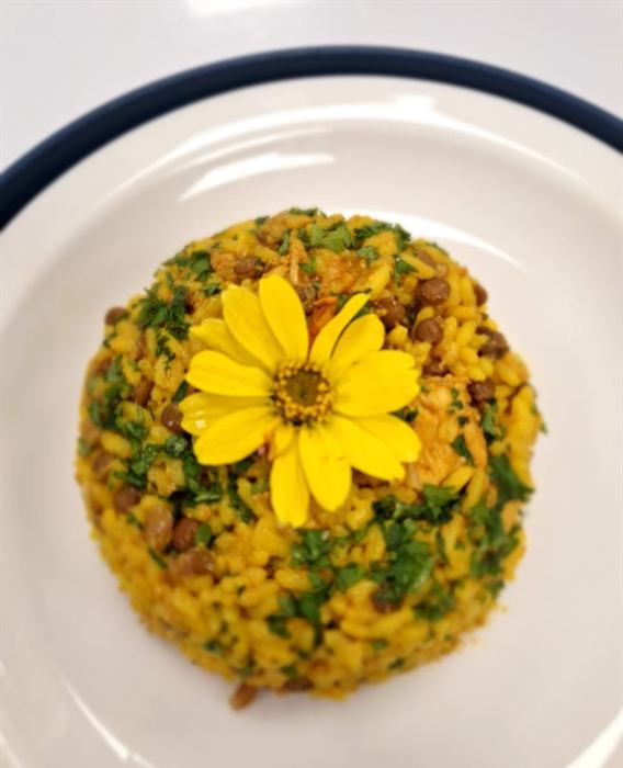 A moulded round of herbed yellow rice topped with a yellow edible flower