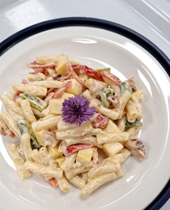 Creamy pasta salad with peppers and herbs, finished with a purple edible flower