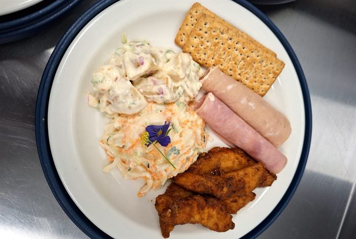 Cold plate of chicken mayonnaise with an edible flower, ham, crackers and a crumbed portion