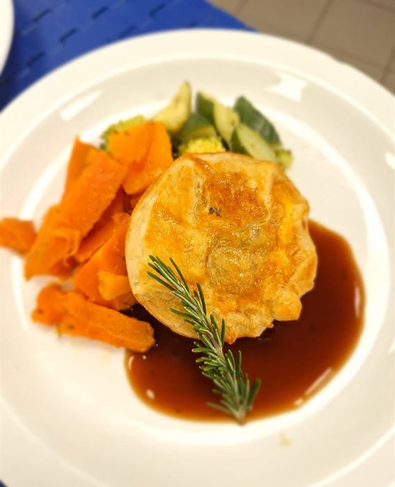 Puff-pastry topped pie on a swipe of dark jus with glazed carrot batons and a rosemary sprig
