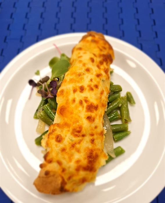A cheese-glazed baked roll resting on a bed of green beans