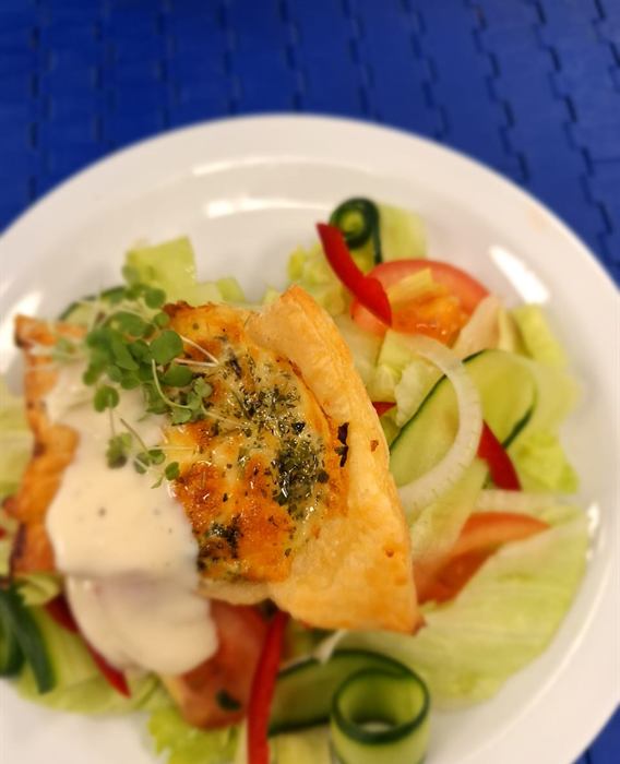Golden pastry parcel with melted cheese and herbs beside a garden salad of tomato, cucumber and peppers