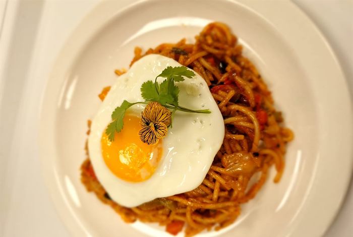 Spaghetti bolognaise crowned with a fried egg and a coriander sprig