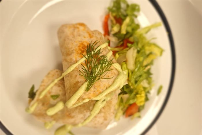 A filled wrap plated with fennel and herb slaw and diced tomato