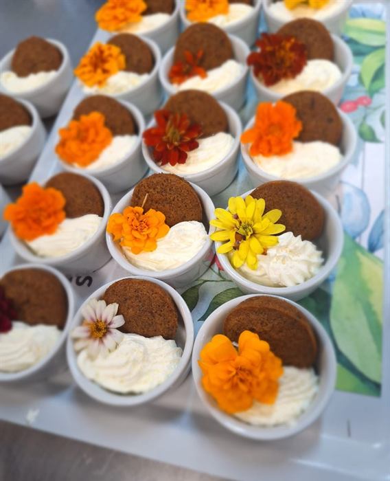 A tray of malva pudding cups with piped cream and orange and yellow edible flowers