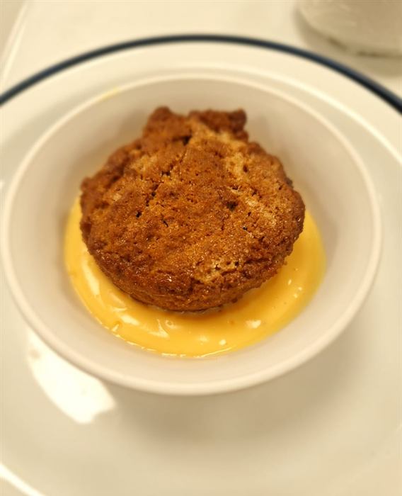 A malva pudding sitting in custard, plated to order
