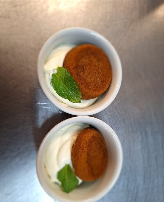 Two malva puddings in custard, each finished with a mint leaf