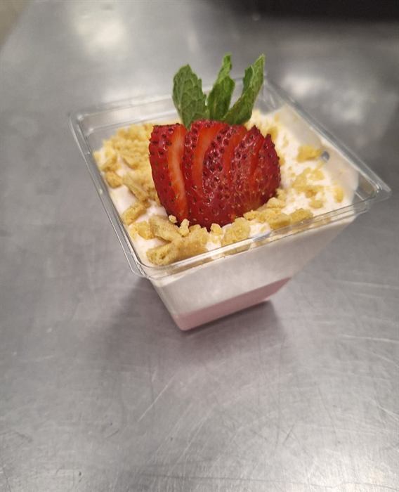 A layered dessert cup topped with a fanned strawberry and mint