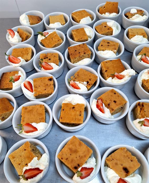 A tray of carrot cake portions with cream and strawberry, plated in bulk
